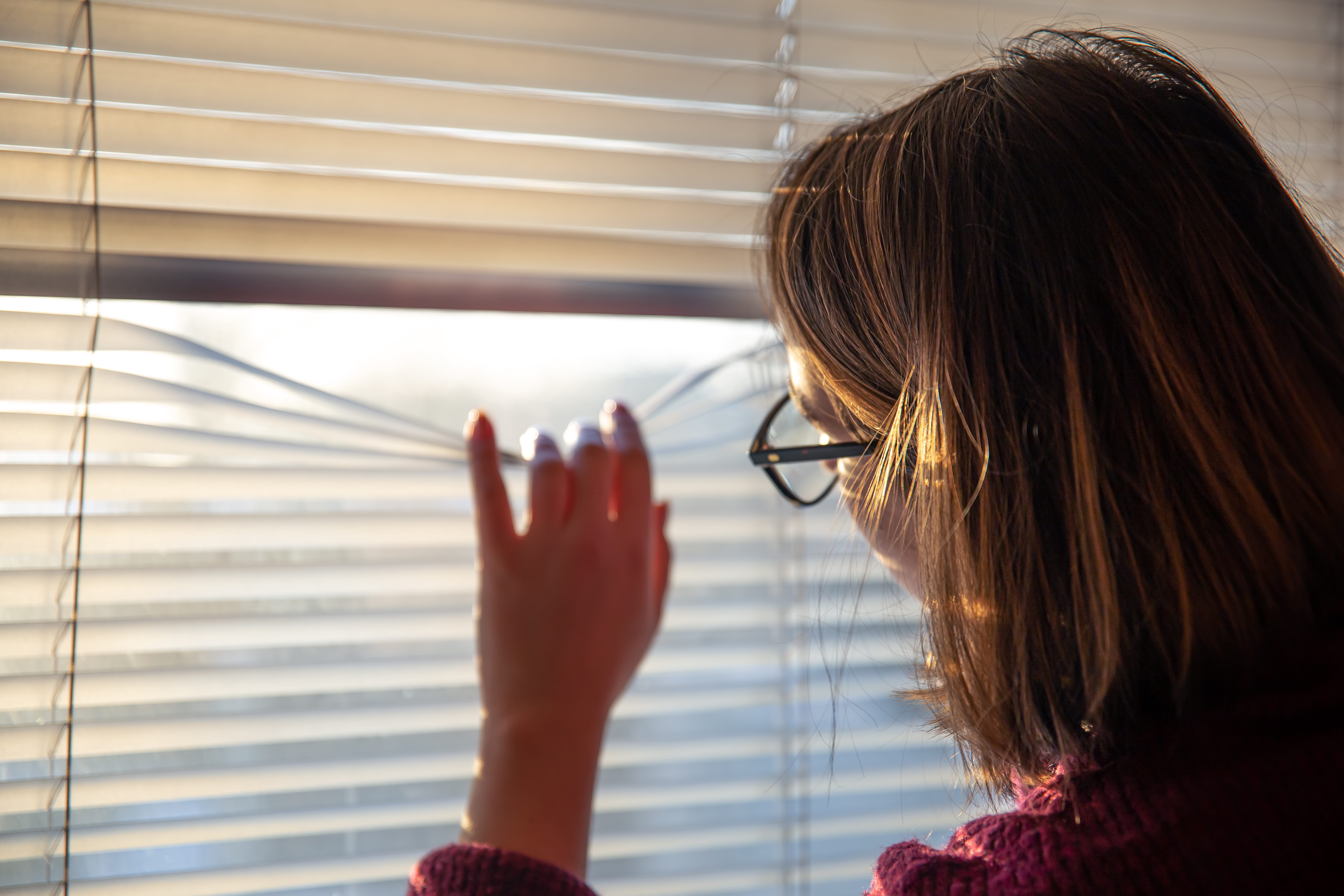 woman-looks-through-blinds-early-morning-sunlight.jpg